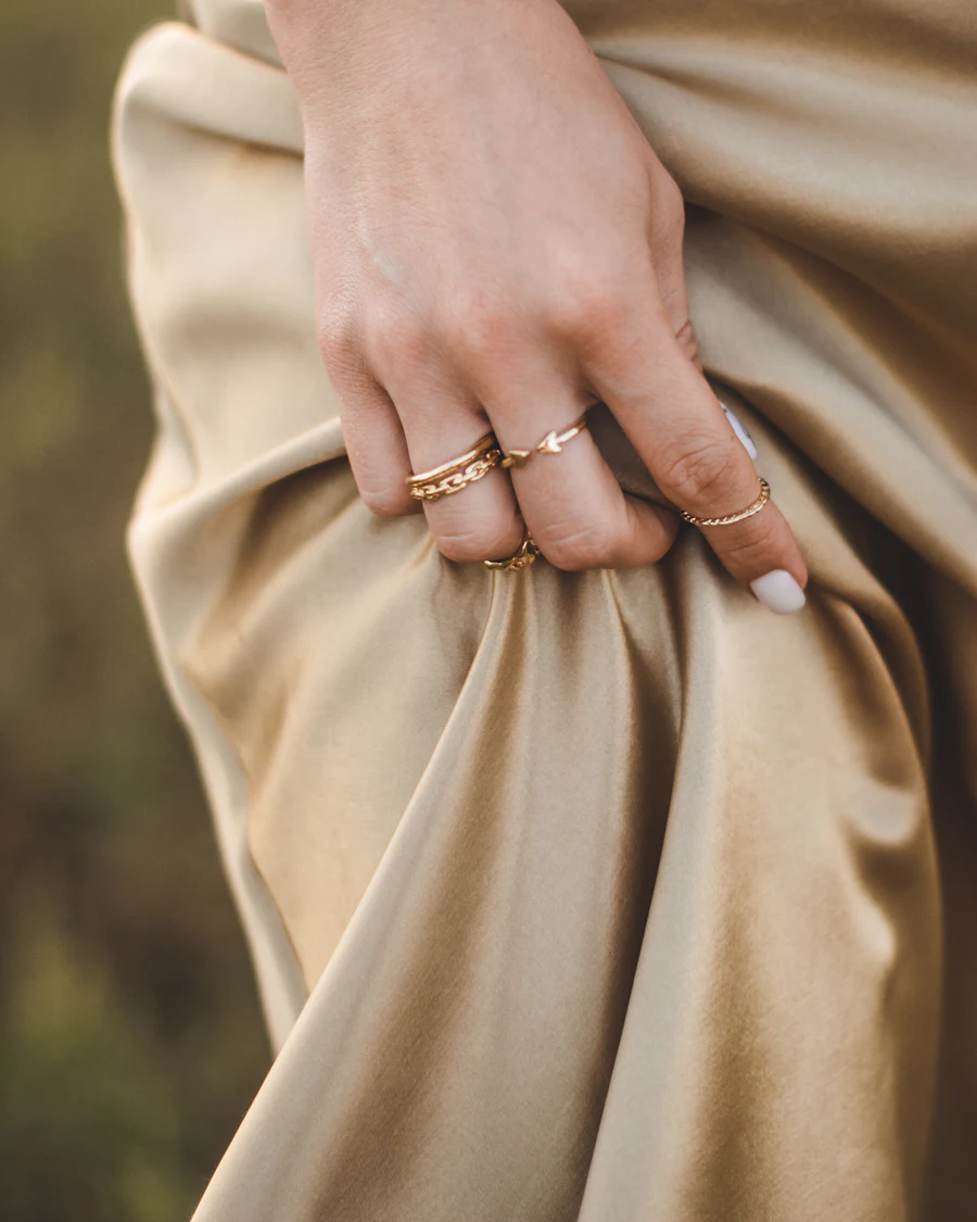A hand wearing thin gold stacking rings against silk