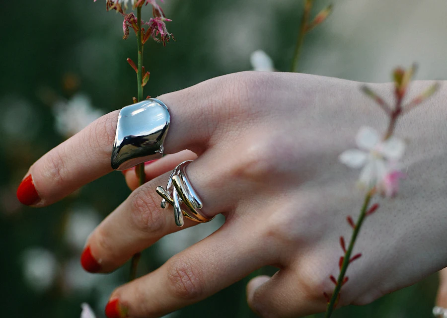 A hand wearing rings among pink flowers